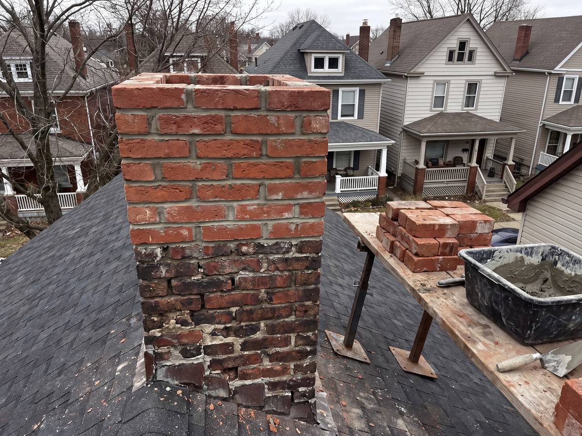 Chimney rebuilt above the roofline in red brick over the old courses, spare bricks and a mortar tub on a roof plank