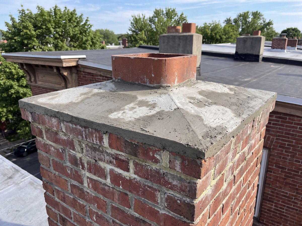 Freshly cast concrete crown on an old brick chimney, still blotchy as it cures, a square clay flue tile rising from it